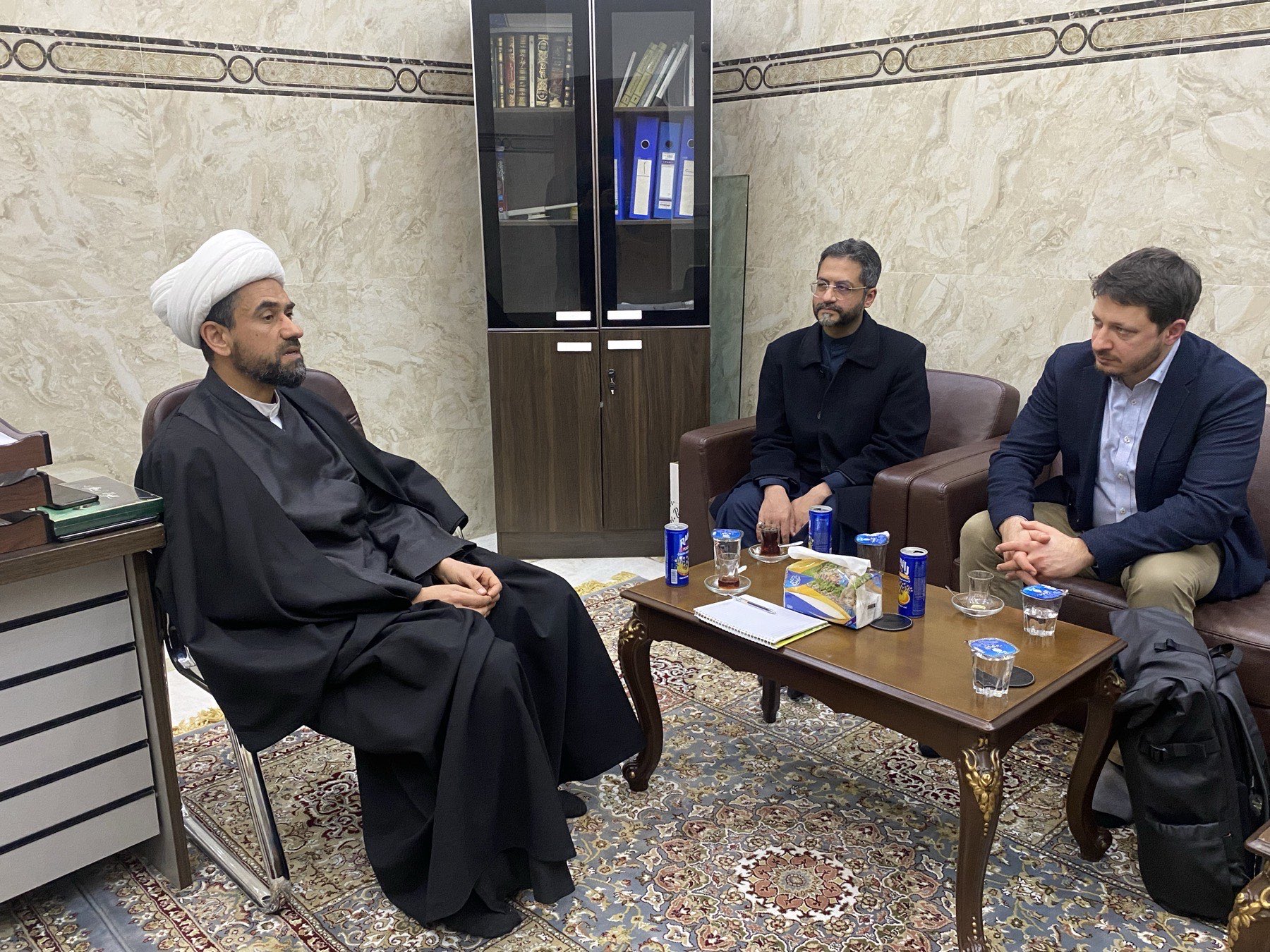 Members of an ICAIR delegation seated in discussion with a scholar, beside a bookcase of bound volumes.