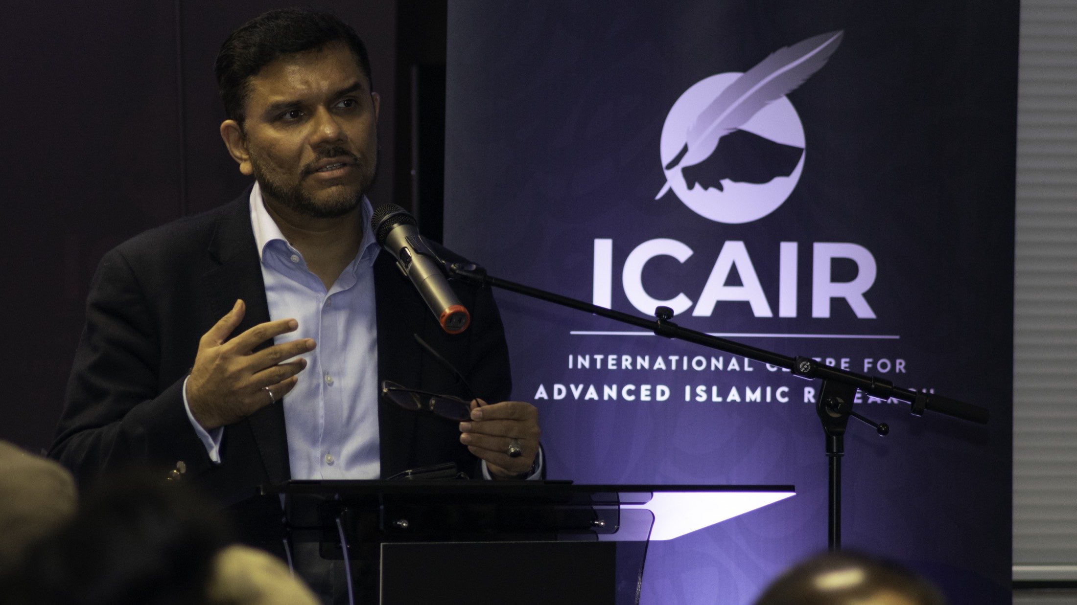 A speaker addressing the ICAIR annual conference from the lectern.