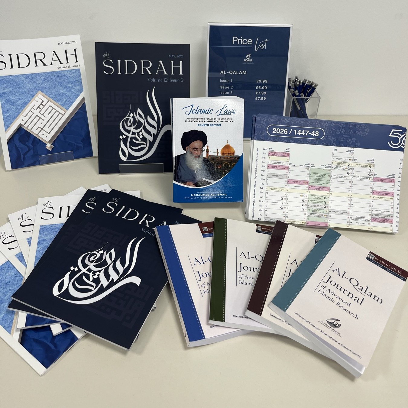 Printed issues of Al-Sidrah magazine and Al-Qalam journal arranged on a table, alongside a price list and a copy of Islamic Laws.
