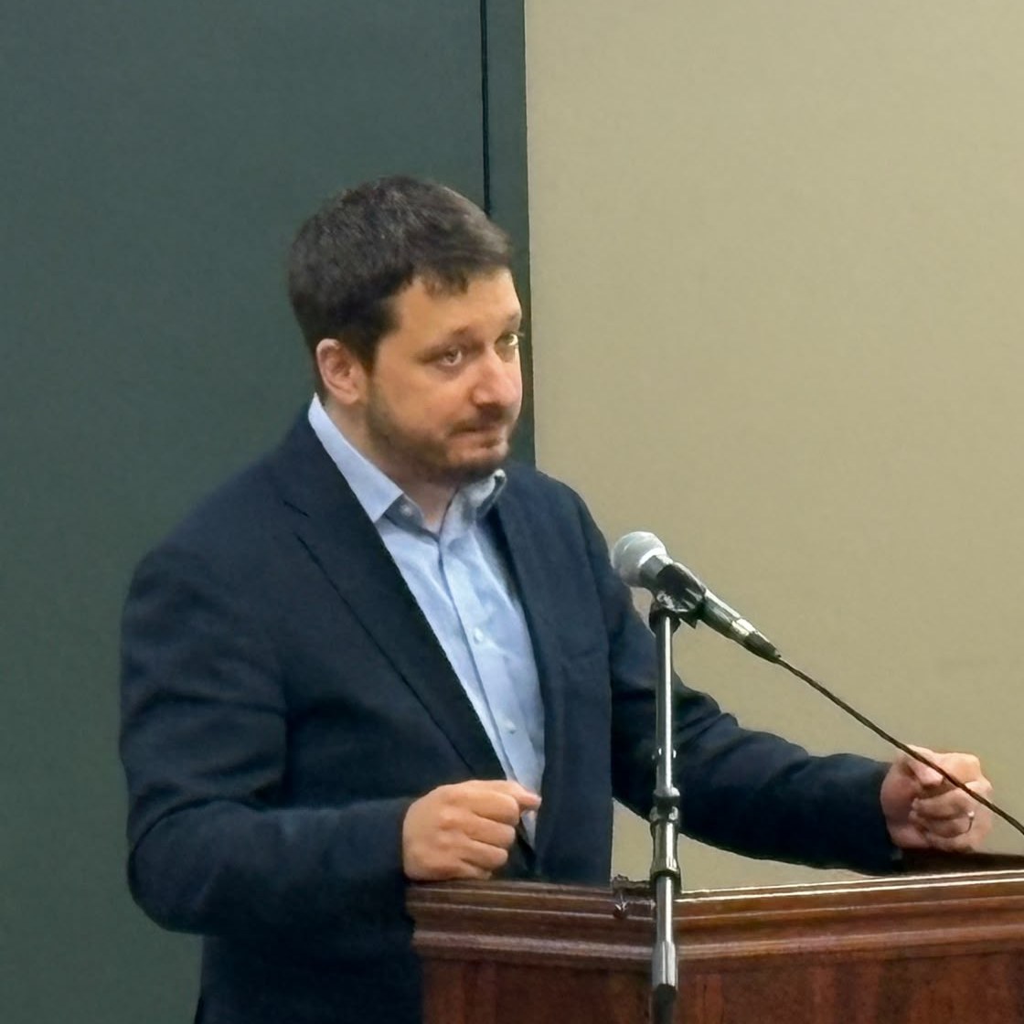 A speaker at the lectern, leaning into the microphone mid-sentence.