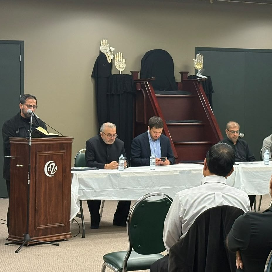 A speaker at the lectern addressing a seated panel and an audience.