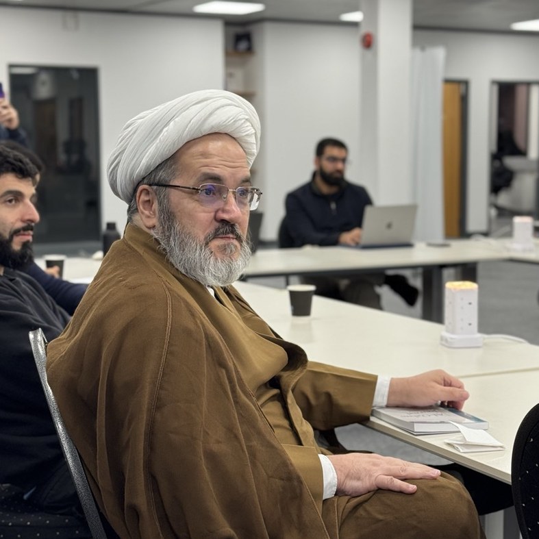 A scholar seated at the table among the participants at the seminar.